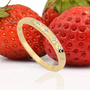 Peut inclure: Une fine bague en or avec cinq petits diamants sertis en rangée. La bague est photographiée sur une surface blanche avec des fraises rouges.