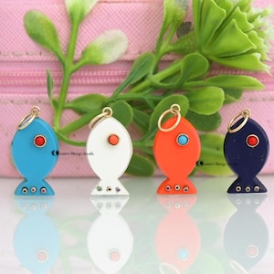 May include: Four colorful fish-shaped pendants. Each pendant has a gold loop at the top and a small, round gemstone for the eye. The fish are blue, white, orange, and navy, with various gemstone accents.