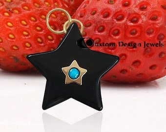 May include: Black star-shaped pendant with a turquoise gemstone in the centre, surrounded by gold accents. The pendant is resting on top of three red strawberries.
