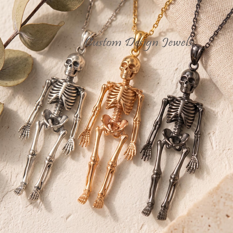 May include: Three skeleton pendants on chains in silver, gold, and dark gunmetal tones. Each pendant features a detailed human skeleton figure with articulated limbs. The text Custom Design Jewels is visible in the center.
