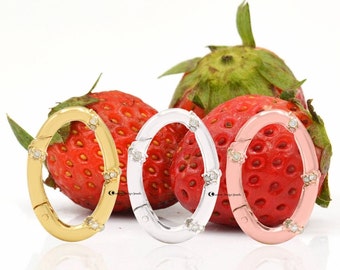 May include: Three oval-shaped clasps with a decorative design of small diamonds. The clasps are gold, silver, and rose gold in color. The clasps are displayed on a background of red strawberries.