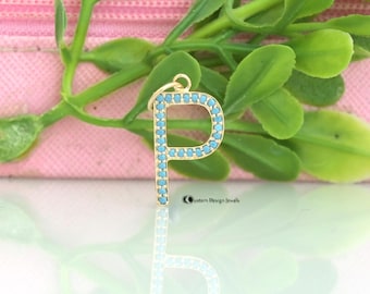 May include: Gold letter P charm with turquoise blue stones. The charm is on a white surface with a pink and green background.