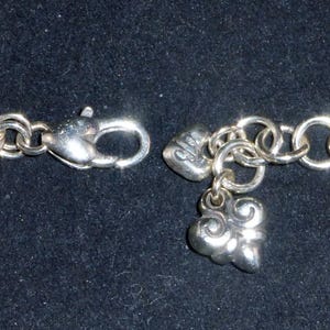 May include: A silver charm bracelet with a heart and a swirl charm. The bracelet is made of a chain link design.