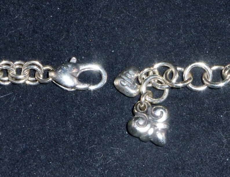 May include: A silver charm bracelet with a heart and a swirl charm. The bracelet is made of a chain link design.