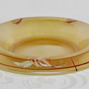 May include: A large, round, amber-colored glass bowl with a decorative design of leaves and flowers in shades of white, red, and brown.
