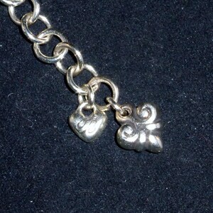 May include: A silver chain bracelet with two charms, one heart-shaped and one with a decorative design.