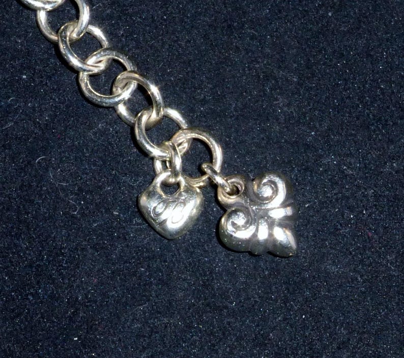 May include: A silver chain bracelet with two charms, one heart-shaped and one with a decorative design.