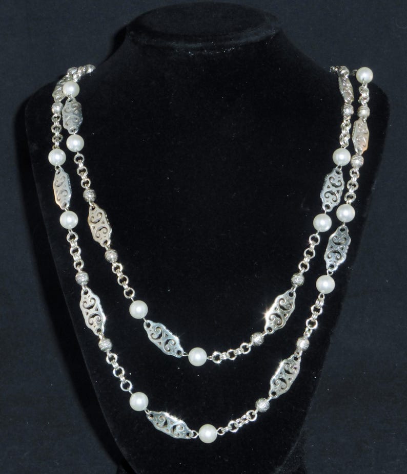 May include: A silver chain necklace with white pearls and a delicate filigree design. The necklace is double-stranded and has a long length.