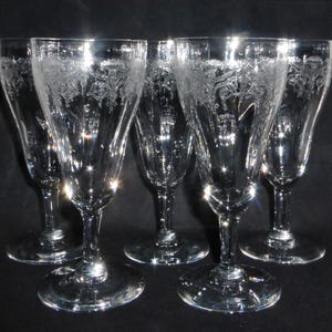 May include: Set of six clear glass wine glasses with a delicate etched floral design. The glasses have a tall, slender stem and a wide bowl.