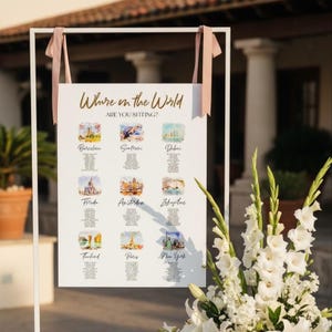 May include: A white rectangular wedding seating chart sign titled Where in the World ARE YOU SITTING? featuring nine watercolor illustrations of global cities including Barcelona, Santorini, Dubai, Florida, Amsterdam, Zakynthos, Thailand, Paris, and New York.