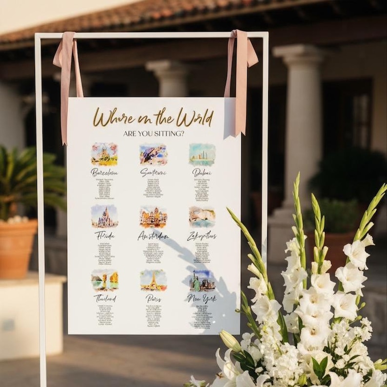 May include: A white rectangular wedding seating chart sign titled Where in the World ARE YOU SITTING? featuring nine watercolor illustrations of global cities including Barcelona, Santorini, Dubai, Florida, Amsterdam, Zakynthos, Thailand, Paris, and New York.