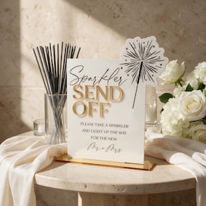 Könnte beinhalten: Ein weißes rechteckiges Acrylschild mit goldener 3D-Beschriftung Sparkler SEND OFF, PLEASE TAKE A SPARKLER AND LIGHT UP THE WAY FOR THE NEW Mr + Mrs und einer schwarzen Strichzeichnung eines Wunderkerzen-Funkens in der oberen rechten Ecke.