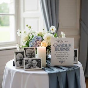 K&ouml;nnte beinhalten: Ein Gedenkdisplay mit einem wei&szlig;en Schild mit dem Text This CANDLE BURNS IN LOVING MEMORY OF THOSE WHO ARE NOT HERE TODAY BUT ARE FOREVER IN OUR hearts, einer brennenden Stumpenkerze, drei wei&szlig;en Bilderrahmen und einem Blumenarrangement.