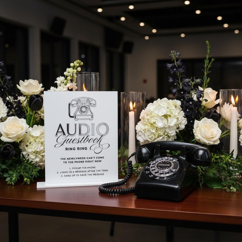 Puede incluir: Un tel&eacute;fono negro vintage con un dial giratorio se encuentra sobre una mesa de madera junto a un letrero que dice "Audio Guestbook". El letrero es blanco con texto negro y un gr&aacute;fico de tel&eacute;fono. Flores blancas y negras y velas rodean el tel&eacute;fono.