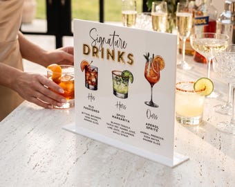 May include: A white acrylic sign featuring the text Signature Drinks in gold and black, with illustrations of an Old Fashioned, Spicy Margarita, and Aperol Spritz. The sign lists ingredients for each cocktail, including bourbon, tequila, and prosecco.