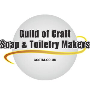 May include: A white circle with a gold curved line around it. The text "Guild of Craft Soap & Toiletry Makers" is in black text on the circle. The text "GCSTM.CO.UK" is in black text below the circle.