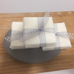 May include: Three bars of white soap wrapped in a grey ribbon with white polka dots. The soap is sitting on a grey circular base.