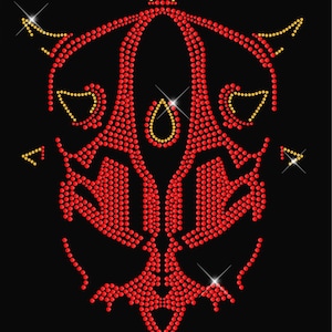 May include: Red and gold rhinestone design of a stylized face with horns. The design is made of small, round rhinestones.