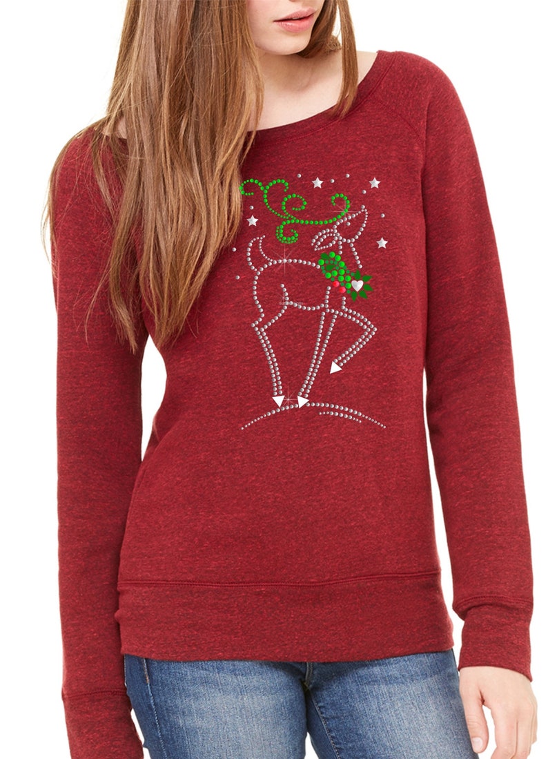 May include: Red long-sleeved sweatshirt with a sparkly reindeer design. The reindeer is wearing a green holly wreath and has a red heart on its nose. The design is surrounded by white stars.