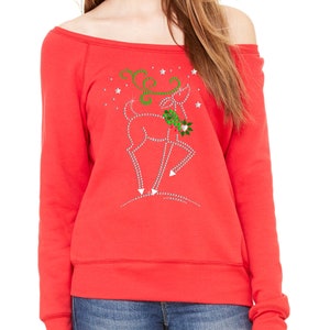 May include: Red off-the-shoulder sweatshirt with a rhinestone reindeer design. The reindeer is holding a sprig of holly and is surrounded by stars.