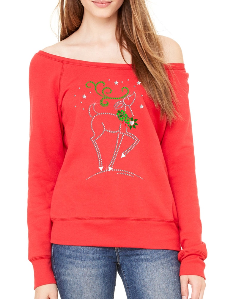 May include: Red off-the-shoulder sweatshirt with a rhinestone reindeer design. The reindeer is holding a sprig of holly and is surrounded by stars.