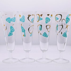Könnte beinhalten: Set aus vier klaren Champagnergläsern mit einem modernen Design aus der Mitte des Jahrhunderts. Die Gläser haben ein geometrisches Muster aus türkisfarbenen und goldenen Formen.