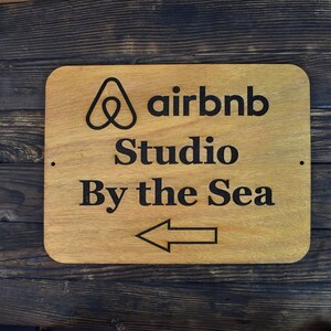 May include: A wooden sign with the Airbnb logo and the text "Studio By the Sea" with an arrow pointing to the left.