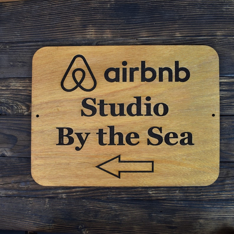 May include: A wooden sign with the Airbnb logo and the text "Studio By the Sea" with an arrow pointing to the left.
