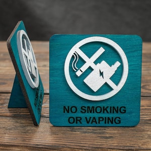 Puede incluir: Dos letreros de madera azul turquesa con un símbolo blanco de prohibido fumar y el texto "NO SMOKING OR VAPING".