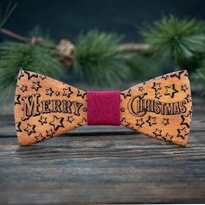 May include: A wooden bow tie with the words "MERRY CHRISTMAS" etched into the wood, surrounded by star shapes. The bow tie has a claret fabric centre and is a festive accessory.