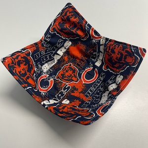 May include: A square fabric bowl with a navy blue background and an orange and white Chicago Bears logo pattern. The bowl is open and appears to be made of quilted fabric.