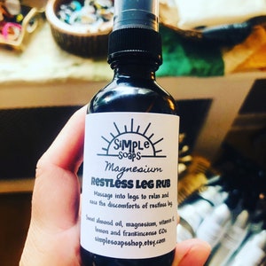 Puede incluir: Una botella de vidrio marrón con una etiqueta blanca que dice "SIMPLE soaps Magnesium RESTLESS LEG RUB Massage into legs to relax and ease the discomforts of restless legs Sweet almond oil, magnesium, vitamin E, lemon and frankincense EOs simplesoapsshop.etsy.com"