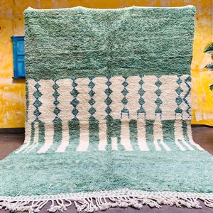 May include: A large, rectangular rug with a textured, shaggy pile. The rug features a color block design with a top section of solid teal, a middle section with white diamonds and teal accents, and a bottom section with teal and white stripes. The rug has a white fringe.