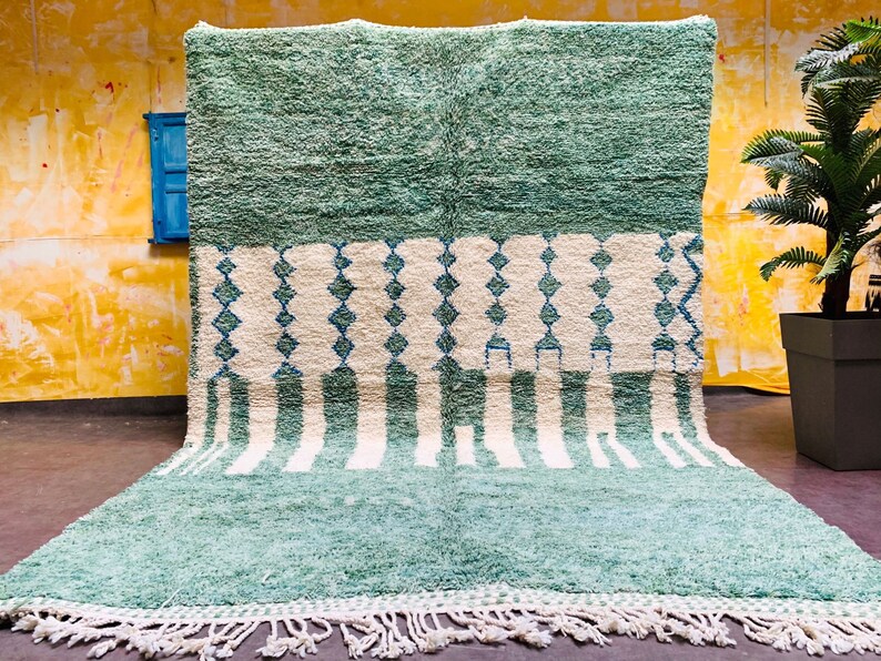 May include: A large, rectangular rug with a textured, shaggy pile. The rug features a color block design with a top section of solid teal, a middle section with white diamonds and teal accents, and a bottom section with teal and white stripes. The rug has a white fringe.