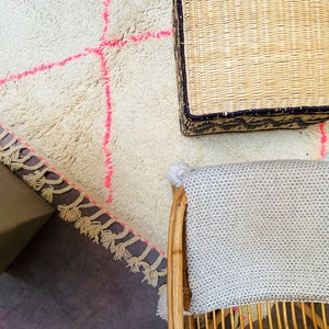 May include: A white fluffy rug with pink stitching and a woven basket with a black trim. A white woven chair with a gray cushion is in the background.