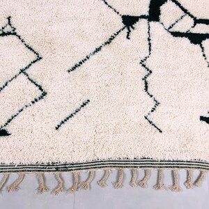 Detail shot of cream Beni Ourain rug displaying black abstract line work and authentic hand-knotted construction