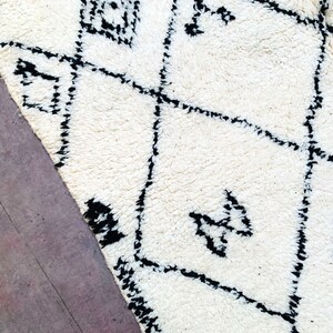 May include: A white rug with a black geometric pattern. The rug has a soft, fluffy texture.