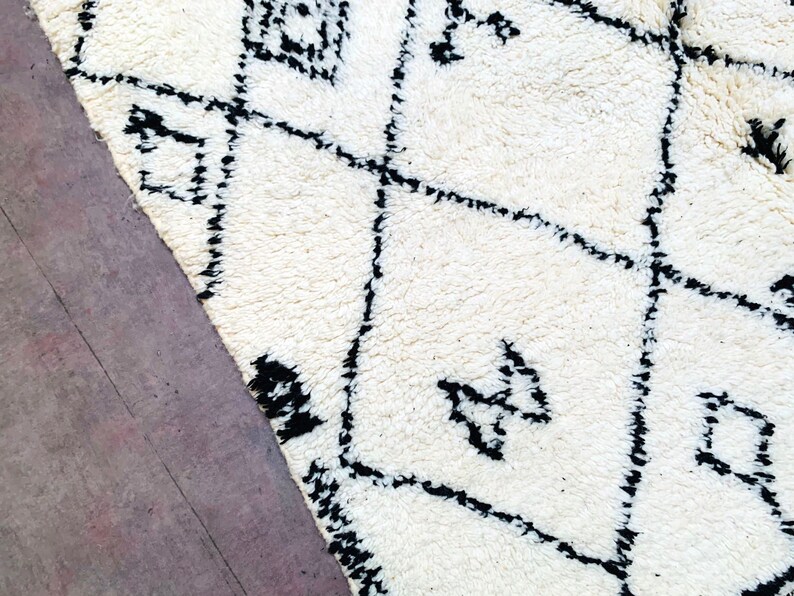 May include: A white rug with a black geometric pattern. The rug has a soft, fluffy texture.