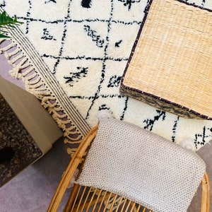 May include: A white and black patterned rug with a woven wicker ottoman and a woven chair with a light grey cushion.