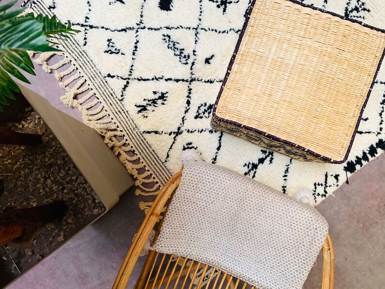 May include: A white and black patterned rug with a woven wicker ottoman and a woven chair with a light grey cushion.