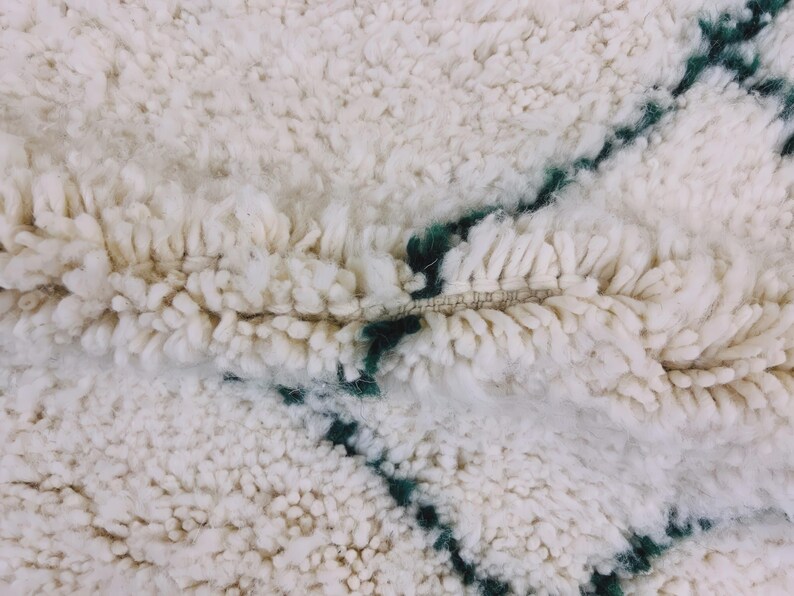 Corner section of cream Beni Ourain rug with black geometric designs and traditional fringe detail work