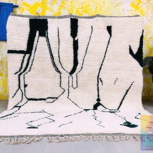 White Beni Ourain rug with black abstract line patterns displayed against colorful yellow and blue background wall