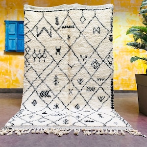May include: A white and black Moroccan rug with a geometric pattern. The rug has a fringe border and is made of wool.