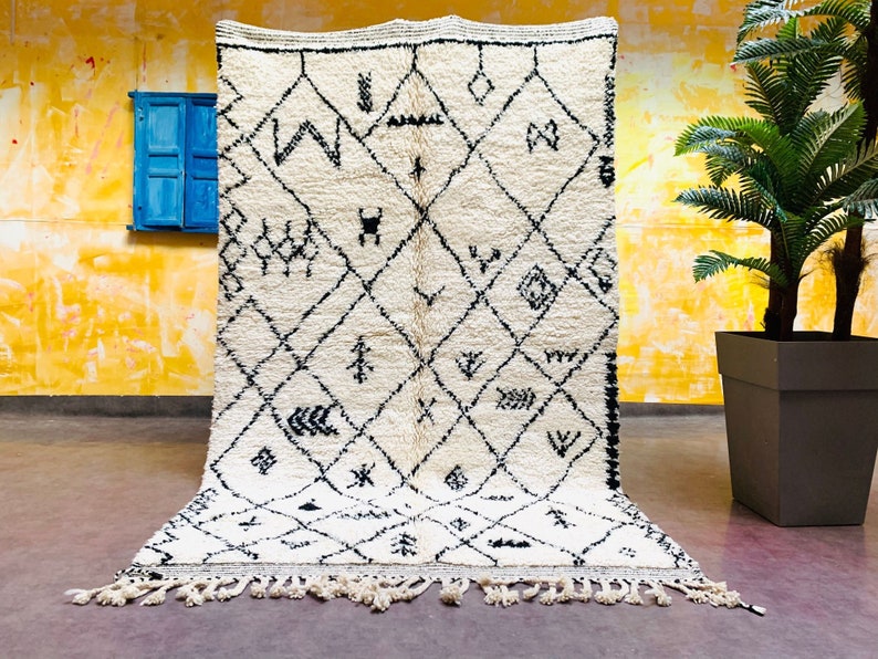 May include: A white and black Moroccan rug with a geometric pattern. The rug has a fringe border and is made of wool.