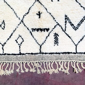 May include: A white rug with a black geometric pattern. The rug has a fringe border.