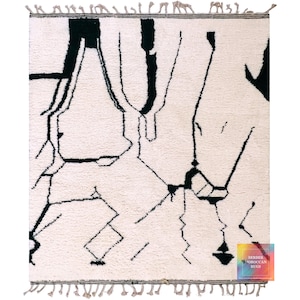 White Beni Ourain rug with black tribal line patterns and traditional fringe edges on neutral surface
