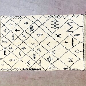 May include: A white Moroccan rug with black geometric patterns and fringe on all sides.