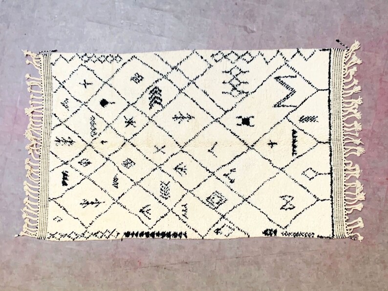 May include: A white Moroccan rug with black geometric patterns and fringe on all sides.