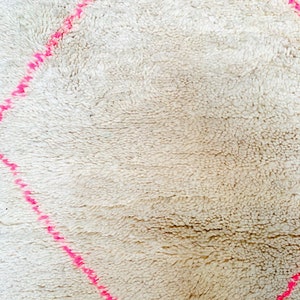 May include: A white rug with a pink diamond pattern. The rug is made of a soft, fluffy material.