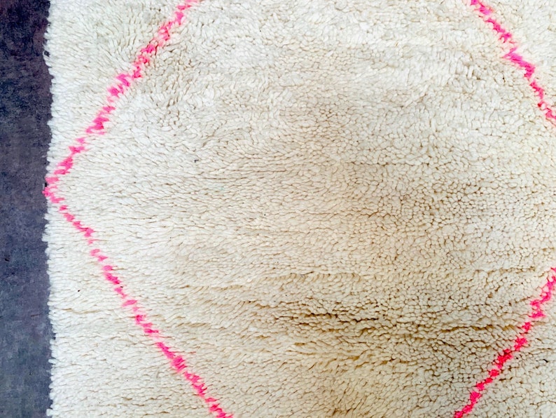 May include: A white rug with a pink diamond pattern. The rug is made of a soft, fluffy material.